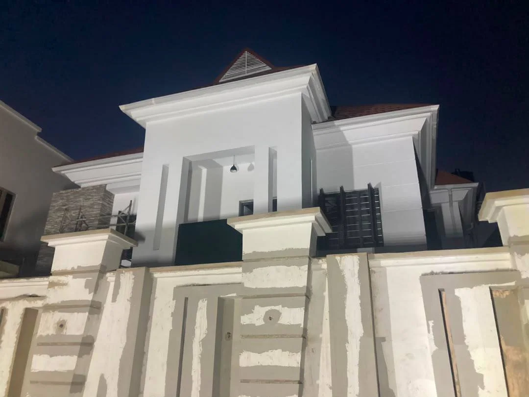 Renovated duplex façade at night, showing the new entrance composition, white exterior finish, dark accent screens, and upgraded boundary wall.