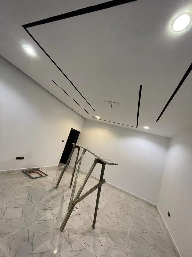 Interior finishing with recessed ceiling lights, black ceiling detailing and marble-pattern floor tiles; temporary work trestles remain.