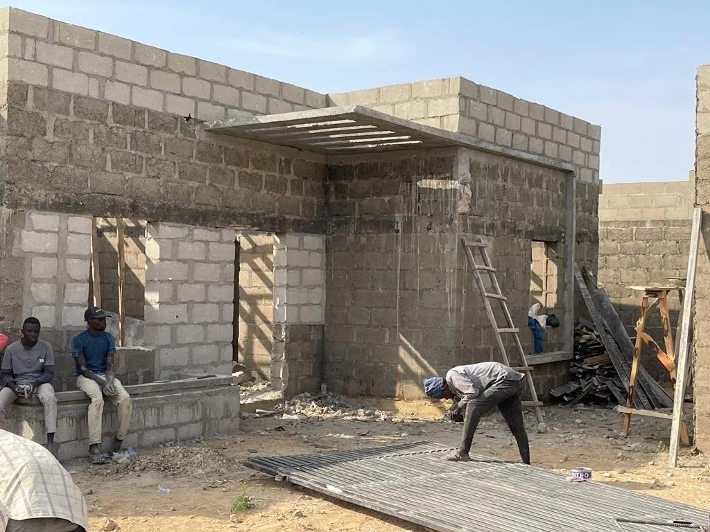 Workers beside a residential unit with exposed masonry, window openings and a concrete entrance canopy.