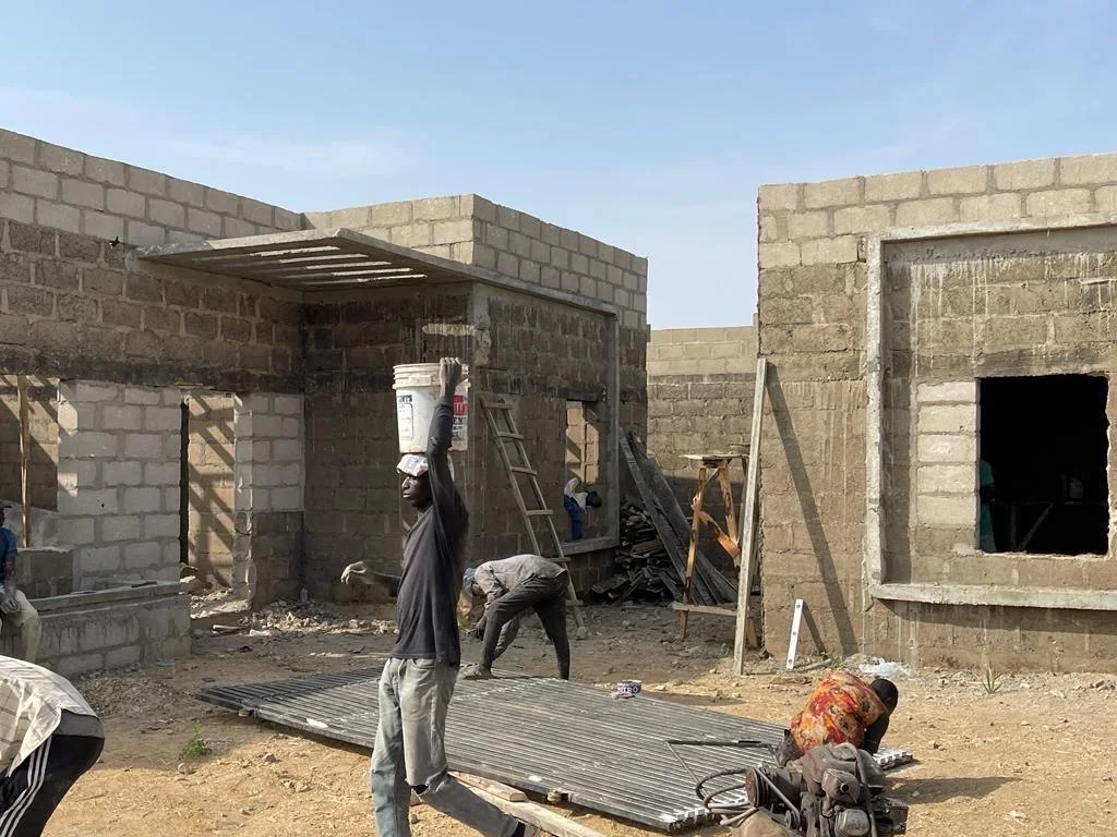 Workers carrying out construction between the compound’s residential units, with exposed blockwork and temporary site equipment.