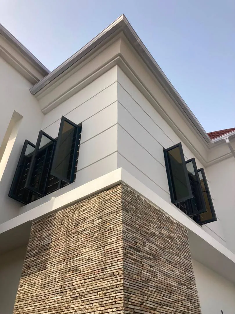 Close-up of the renovated duplex façade showing white wall finishes, dark window screens, projecting roof details, and textured stone cladding.