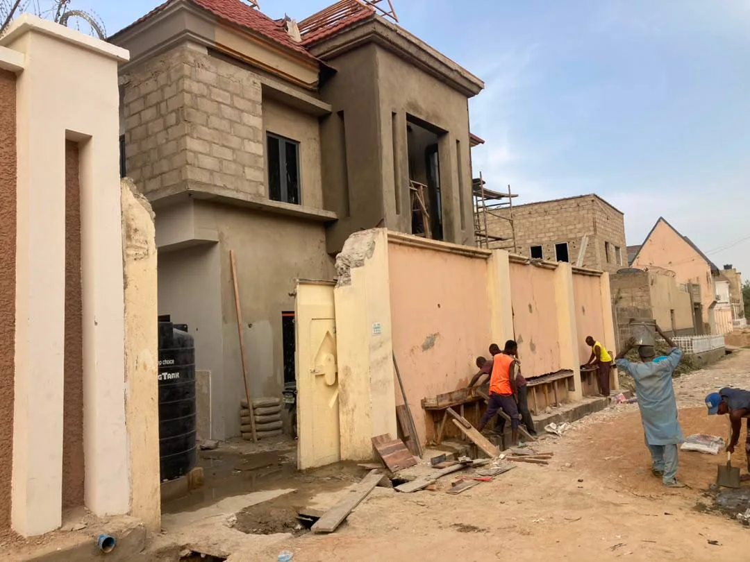 Renovation-stage view of the duplex showing partially reconstructed façade elements, new wall extensions, workers on site, temporary supports, and unfinished external surfaces.
