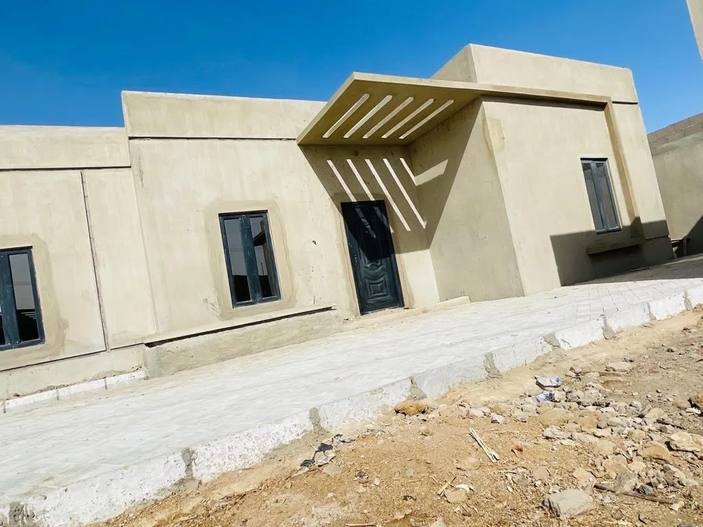 Residential unit during external finishing, showing rendered walls, fitted windows, an entrance door and a slatted canopy.
